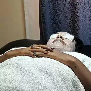 A client lays on a table with her face covered in a mask during a deep-cleansing facial treatment at her home in Syokimau