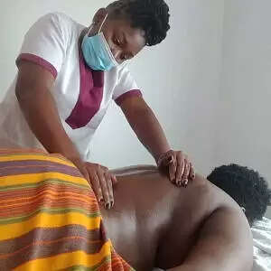 A mobile massage therapist uses the palms to apply deep pressure on the lower-back muscles of the client in Nairobi. Client lays on their stomach on a massage table