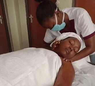 A massage therapist gently twisting the neck muscles of a client in Nairobi. Client lays on her back on a massage table.